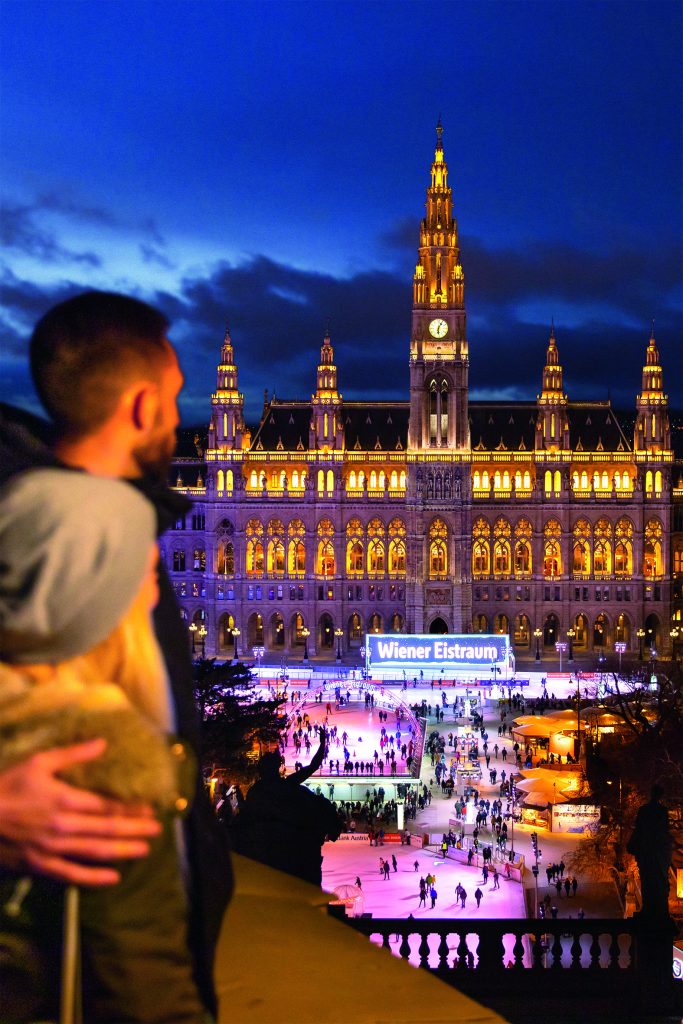 Ein Pärchen steht Arm in Arm vor der Kulisse des Wiener Eistraum auf dem Rathausplatz
