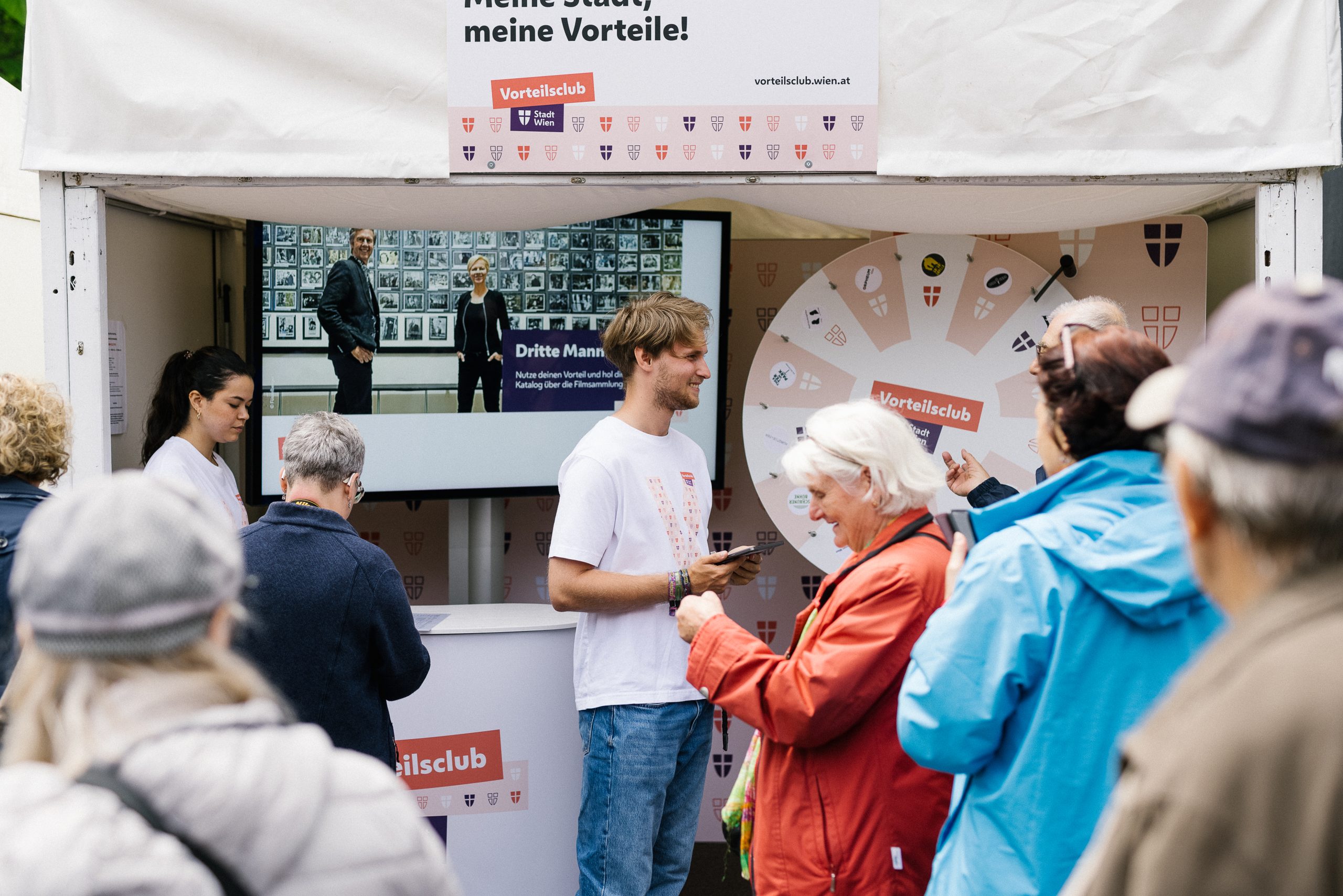 Personen vor einem Vorteilsclub Stand mit einem Glücksrad.
