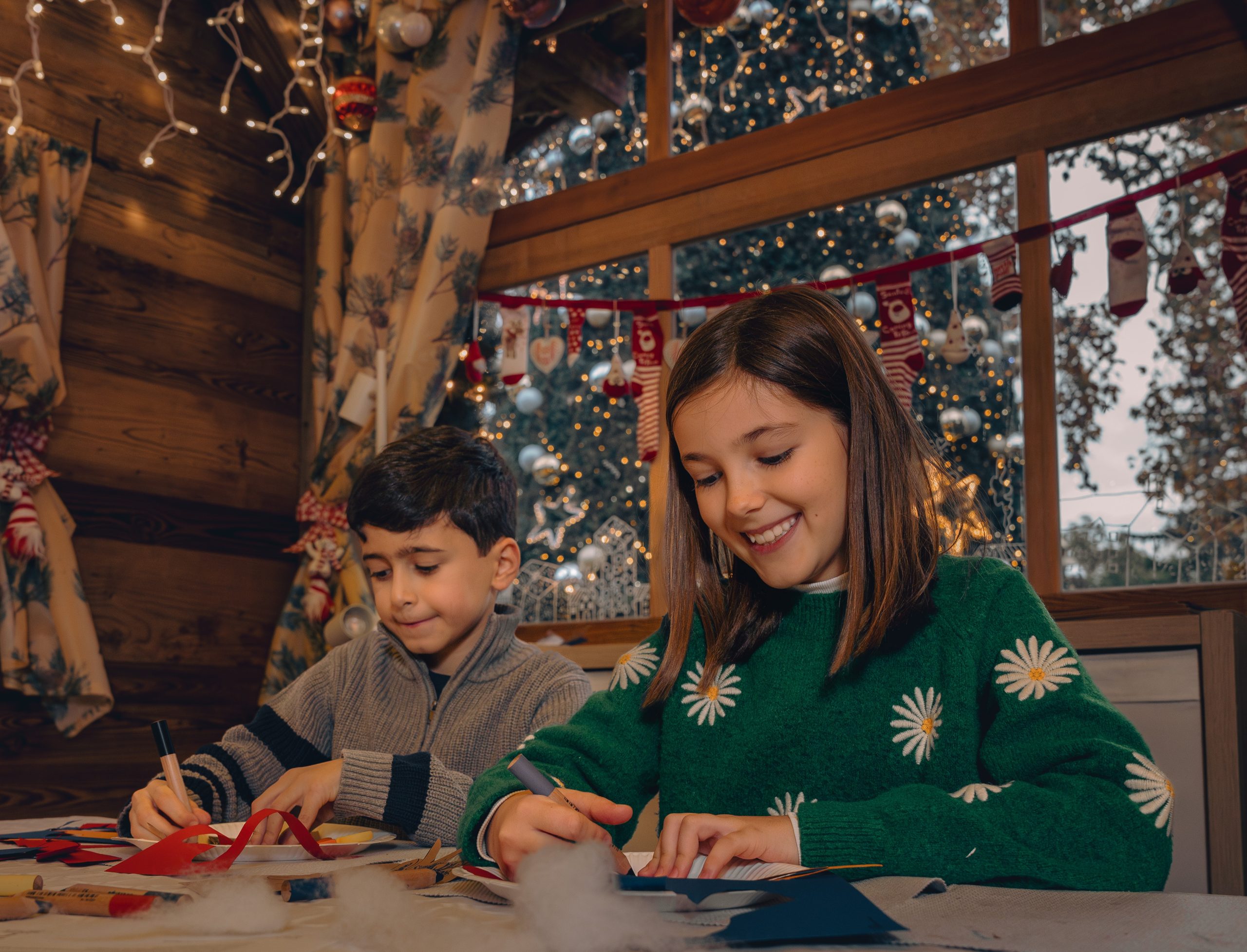 Nahaufnahme von zwei Kindern beim Malen. Der Hintergrund ist weihnachtlich dekoriert.