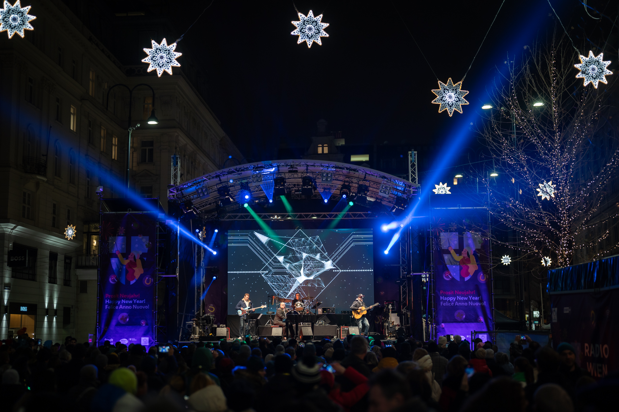 Bühne bei Nacht beim Wiener Silvesterpfad mit Lasershow und Menschenmenge.