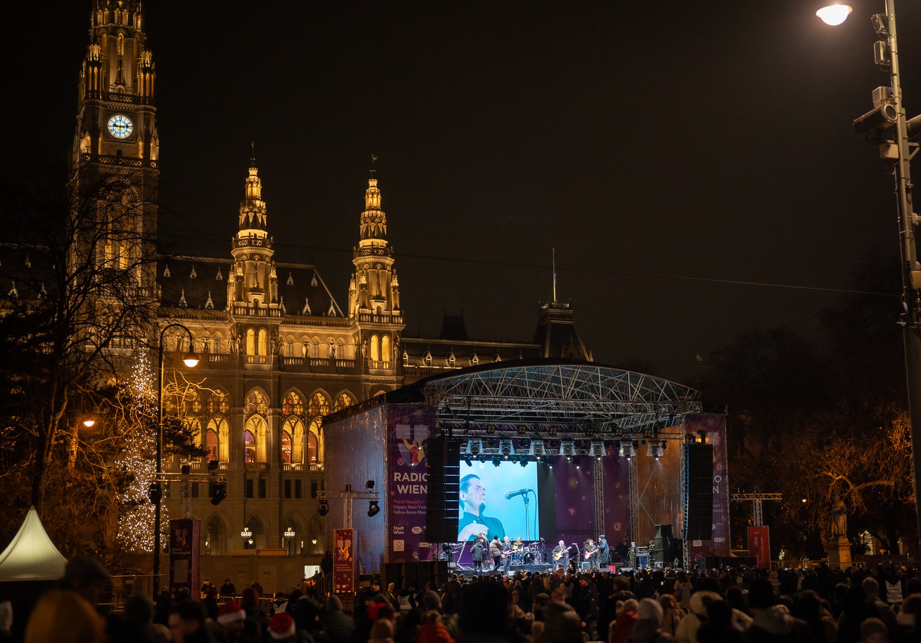Sicht auf das Wiener Rathaus bei Nacht mit einer großen Bühne und Menschenmenge beim Wiener Silvesterpfad.