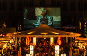 Teil eines aufgesplitteten Fotos des Rathaus und Platz. Auf diesem ist die große Leinwand vom Film Festival und ein großer Sonnenschirm mit Publikum zu sehen.