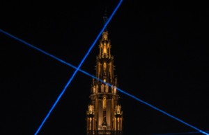 Teil eines aufgesplitteten Fotos des Rathaus. Auf diesem ist die Turmspitze bei Nacht zusehen. Das Rathaus ist erleuchtet und es sind Laser zu sehen.
