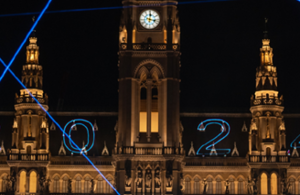 Teil eines aufgesplitteten Fotos des Rathaus. Auf diesem ist die Mitte des Turms bei Nacht zusehen. Das Rathaus ist erleuchtet und es sind Laser zu sehen. Die Zahlen 0 & 2 sind mit einem Laser auf das Rathaus projiziert.