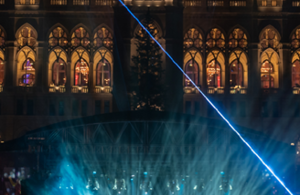 Teil eines aufgesplitteten Fotos des Rathaus. Auf diesem ist die Mitte des Rathaus bei Nacht zusehen. Das Rathaus ist erleuchtet und es findet eine Lasershow vor der Bühne statt. Das Licht ist blau.