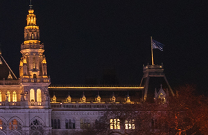 Teil eines aufgesplitteten Fotos des Rathaus. Auf diesem ist die rechte Seite des Dachs mit Türmen und Fahnen zu sehen. Das Rathaus ist beleuchtet.