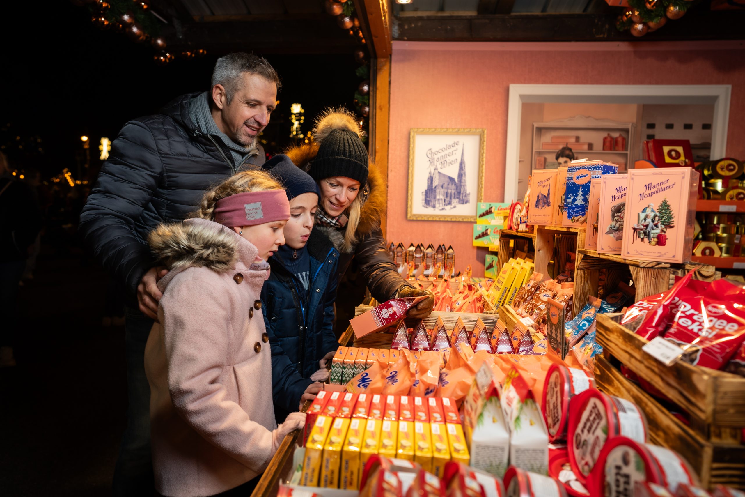 © stadt wien marketing / David Bohmann Eine vierköpfige Familie steht vor einem Manner Marktstand und schaut die vielen verschiedenen Produkte an.